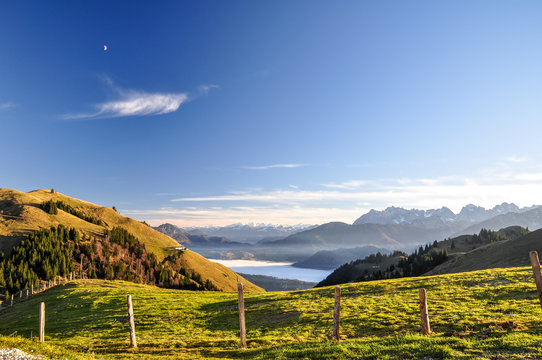Beautiful evening view near Wandberg mountain in the Chiemgau Alps mountain range in Austria. Tranquil scene with a fence, a fresh lawn and mountains in the background and fog in the lowland. 