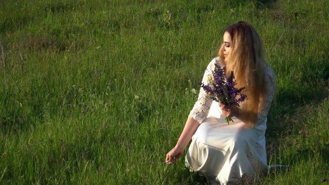 Beautiful young woman walking on the meadow with flowers on the sunset