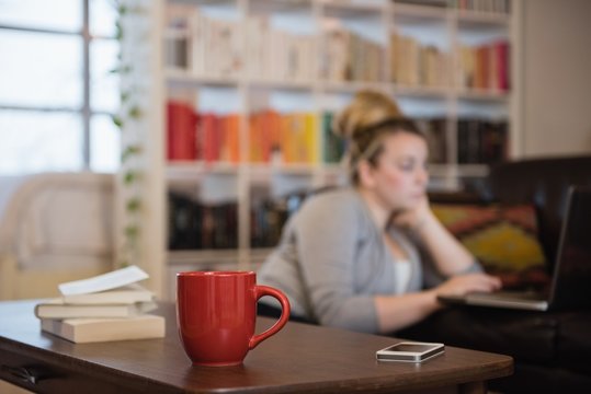 Books, mobile phone and coffee cup on table with woman in background