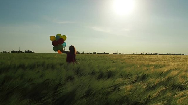 Girl in a field of wheat with balloons. Silhouette of a girl with balloons.