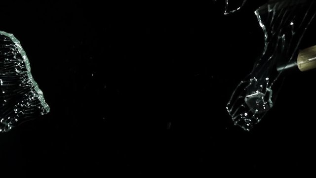 Brings a hammer to the glass and hits it, it crumbles into small pieces. Black background. Slow motion