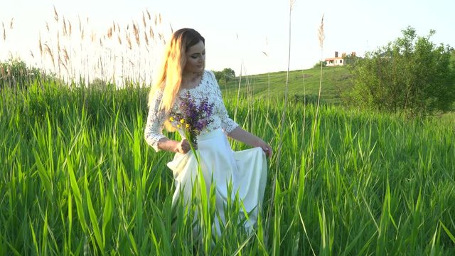 Beautiful woman in white dress walking in the grass on the meadow