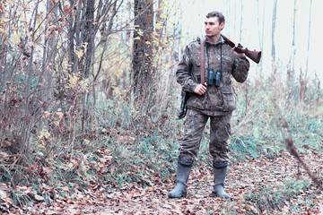 A man in camouflage and with a hunting rifle in a forest on a spring hunt