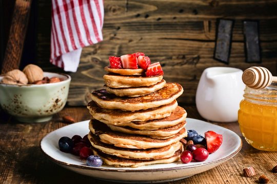 Whole meal pancakes with fresh berries and honey on wooden table. Closeup view. Rustic style stock food photo
