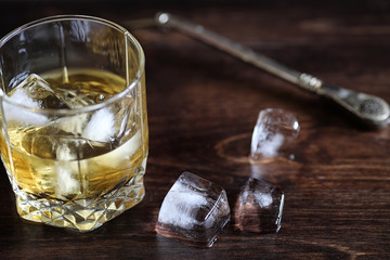 Whiskey in a glass and pieces of ice on a wood