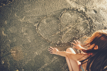 Girl drawing heart in the sand