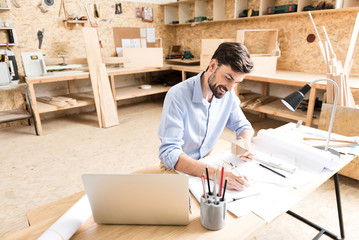 Cheerful bearded craftsman working on new manufacture design in workshop