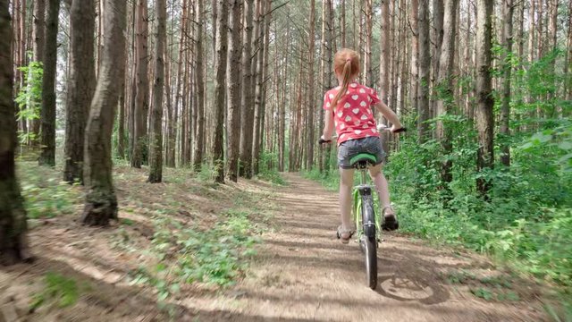 Little girl quickly rides a bicycle on a forest road