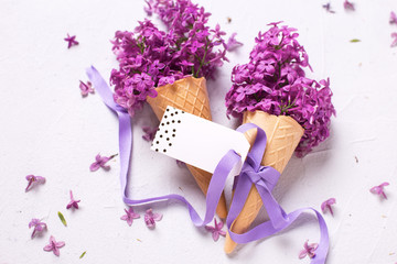 Fresh lilac flowers in waffle cones with ribbon and empty tag
