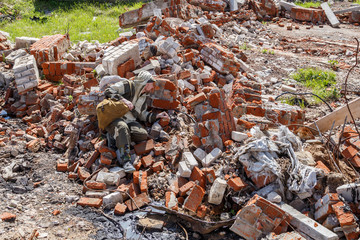 A man in military uniform with a backpack is hiding among the broken brick