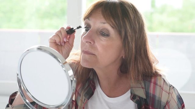 Mature woman applying mascara on eyelashes