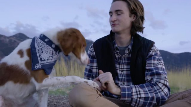 Outdoorsman Gives His Adventure Dog A Treat, Pets Her, Beautiful Mountains In Background