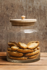 Galletas de pan tostado dentro de un frasco de cristal con tapa de madera sobre un fondo rústico. Vista de frente y de cerca. Formato vertical