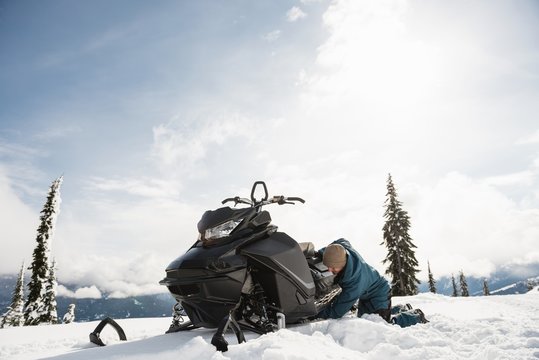 Man repairing snowmobile in snowy alps