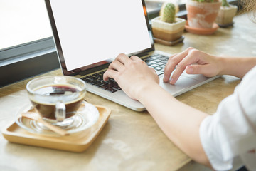 Girl using laptop and showing a blank screen sitting on a couch in the living room with glass of hot coffee at home with a warm light in the background