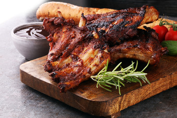 Spicy hot grilled spare ribs from a summer BBQ served with fresh tomatoes on an old vintage wooden cutting board