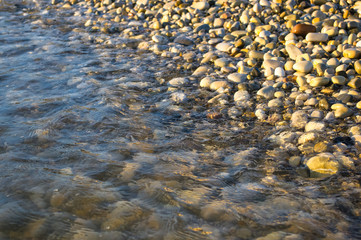 sea pebble beach with multicoloured stones, waves with foam