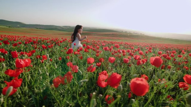 little Asian girl in a white dress running through field of red poppies slow motion, sunset