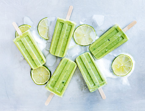 Yogurt and lime popsicles on ice cubes over gray tray background. Refreshing and Healthy summer dessert