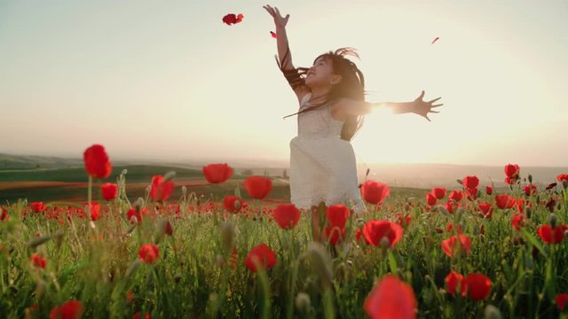 ittle Asian girl in white dress having fun in a field of red poppies in Sunny day, slow motion