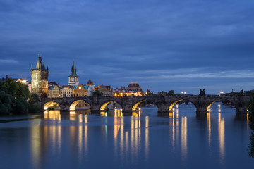 Lit Old Town Bridge Tower, other old buildings and Charles Bridge (Karluv most) and their reflections on the Vltava River in Prague, Czech Republic, at dusk. Copy space.