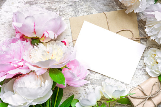 blank white greeting card and envelope with gift box in frame of peonies and roses flowers
