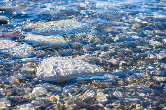 Fototapeta sea pebble beach with multicoloured stones, waves with foam