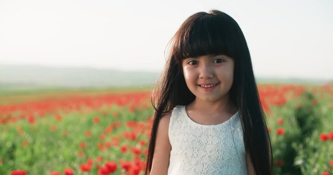 close-up portrait of a little Asian girl in white dress in field of red poppies on a Sunny spring day