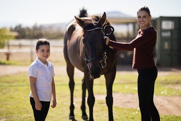 Mother and daughter standing with a brown horse in the ranch