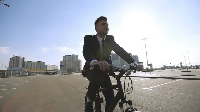 Young businessman in a suit riding a bicycle in the city on a sunny warm weather.
