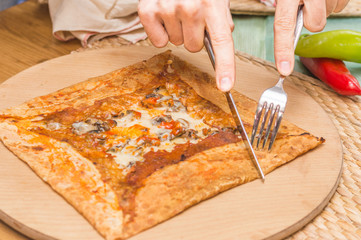 Caucasian man hand cutting crepe with mushroom on wooden cutting board