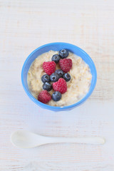 Oatmeal porridge with blueberries and raspberries in bowl - healthy rustic breakfast for kids