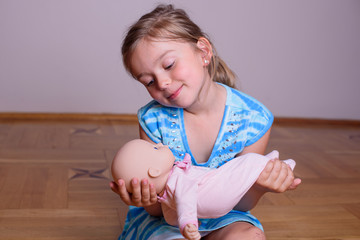 Little girl playing with her baby doll and pretending mom