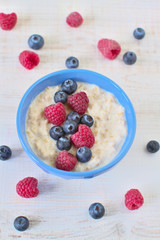 Oatmeal porridge with blueberries and raspberries in bowl - healthy rustic breakfast for kids