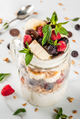 Summer fruit berry breakfast. Healthy banana split breakfast with cream cheese, raspberries, blackberries, mint, white and pink chocolate. In mason jar, marble table. Copy space close view