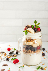 Summer fruit berry breakfast. Healthy banana split breakfast with cream cheese, raspberries, blackberries, mint, white and pink chocolate. In mason jar, marble table. Copy space