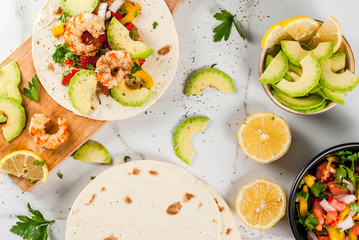 Seafood. Mexican food. Tortilla tacos with traditional homemade salsa salad, parsley, fresh lemon, avocado and grilled shrimp pawns. On a white marble background. Top view copy space