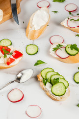 Healthy food. Spring, summer snacks. Sandwiches toast with homemade cream cheese and fresh vegetables - radish, cucumber, tomatoes, onion, pepper. On a white marble table.