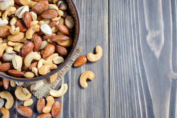 Mixed nuts spilling out of bowl on wooden table. Macro still-life with shallow dof