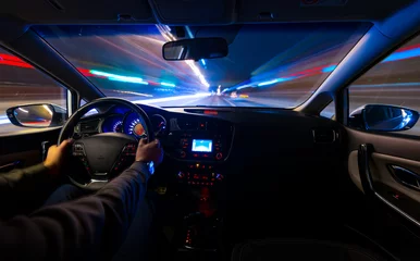 Foto auf Acrylglas Schnelle Autos Mit den Händen am Steuer bewegt sich das Auto nachts mit hoher Geschwindigkeit auf der Autobahn. Verschwommene Straße mit Lichtern mit einem Auto mit hoher Geschwindigkeit.
