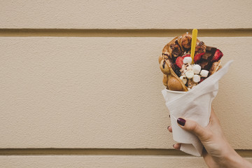 Hand holding bubble waffle with fruits, chocolate and marshmallow, with copy space