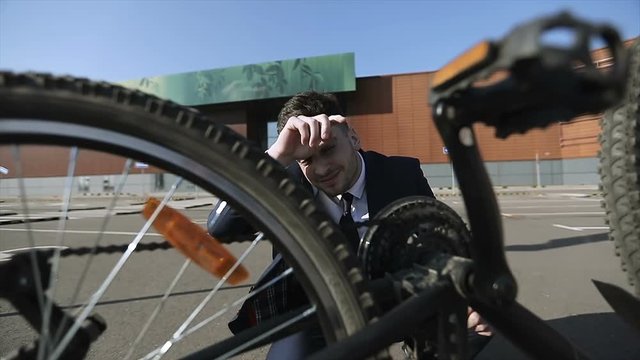 Tired businessman in a suit can not fix or repair a bicycle.
