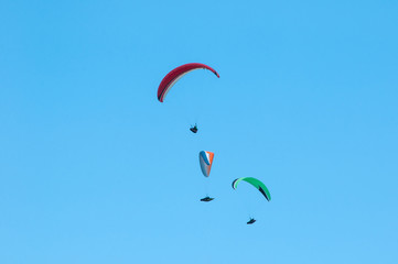 Three paragliders fly in the sky in the sunny day.