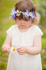 toddler girl with a wreath of flowers guesses on a chamomile