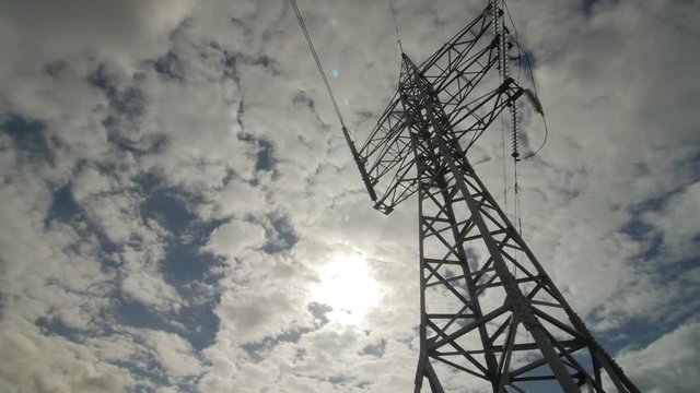 High-voltage tower with high voltage wires, clouds in the sky.