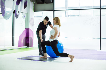 Senior woman with personal trainer exercise with ball