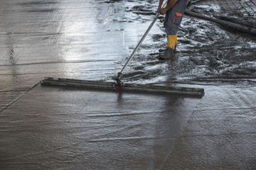 Worker leveling fresh poured concrete floor with a channel float
