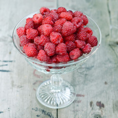 Fresh ripe raspberries in crystal vase on old rustic wooden table