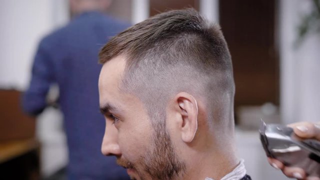 Hand of unrecognizable barber using trimmer on head of stylish client in salon