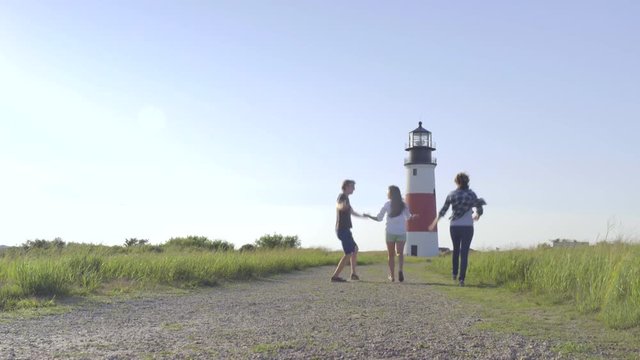 Excited Multiethnic Group Of Teens Run, Twirl, Toward Picturesque Lighthouse